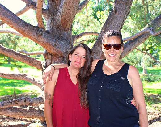 Two women standing next to a tree in front of a forest.