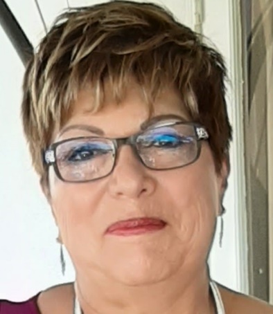 A woman with short hair and glasses is smiling.