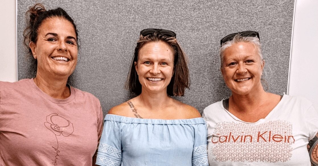 Three women smiling for a picture in front of a wall.